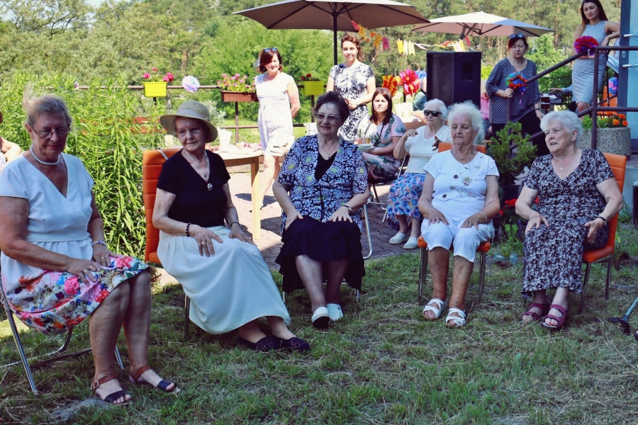 Grupa Seniorek siedzących na krzesłach na tle zieleni. 