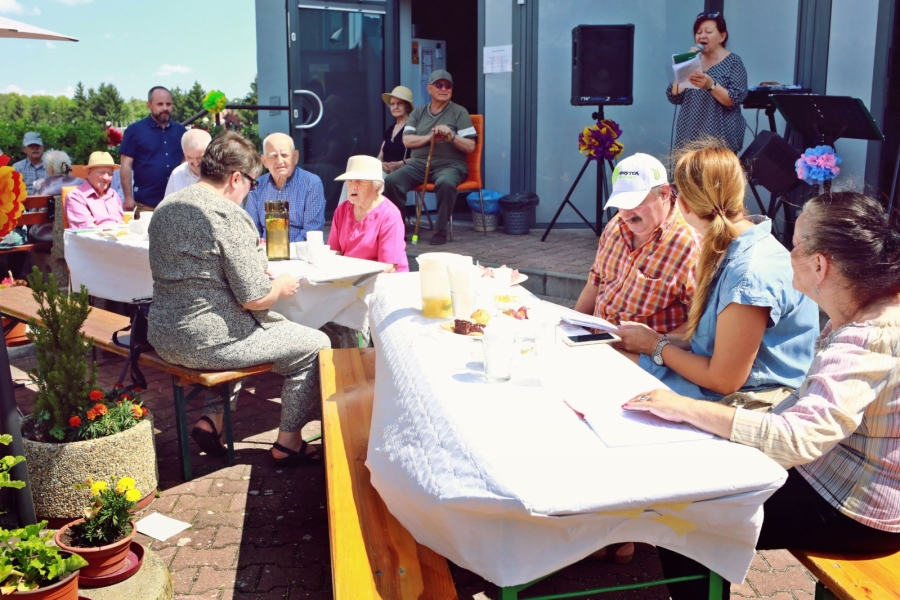 Grupa Seniorów siedzących słuchających wystąpienia muzycznego przy stole.