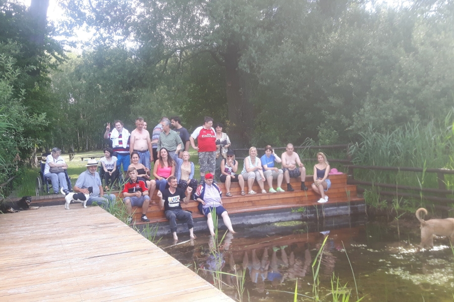 Uczestnicy ŚDS siedzą nad brzegiem zbiornika wodnego.