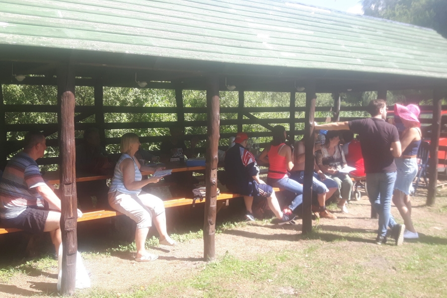 Grupa uczestników chroni się przed słońcem pod altaną.