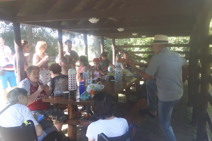 Grupa uczestników spożywając posiłek słucha gry na gitarze pod altaną.