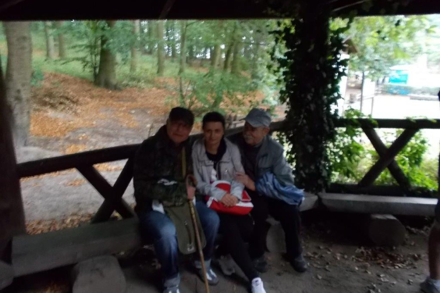 Dwójka uczestników wraz z terapeutką siedzących na ławce pod altaną