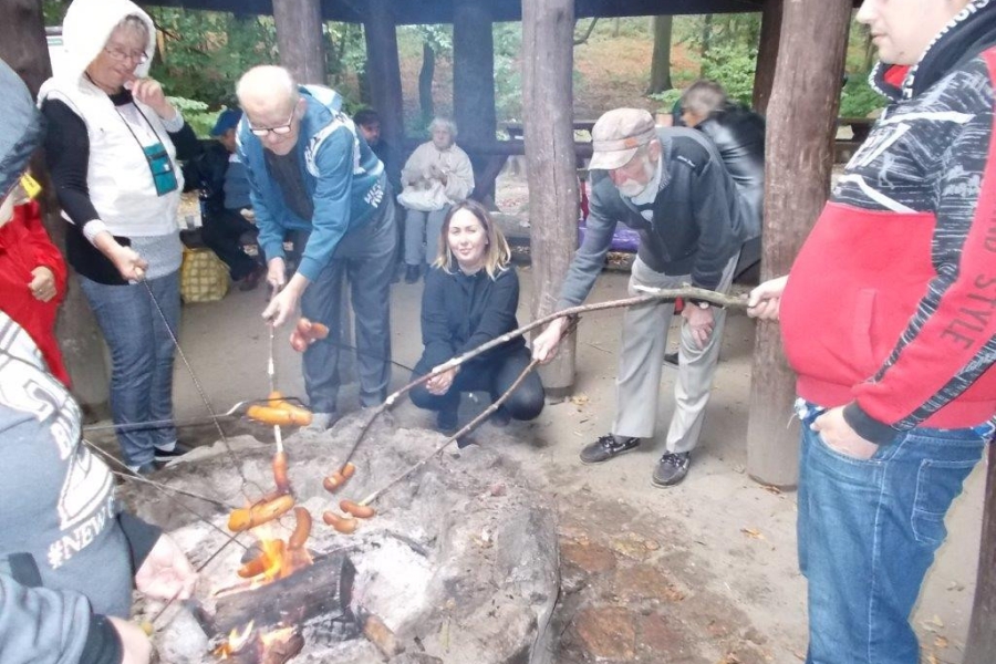 Uczestnicy z terapeutką pieczący kiełbaski nad ogniskiem