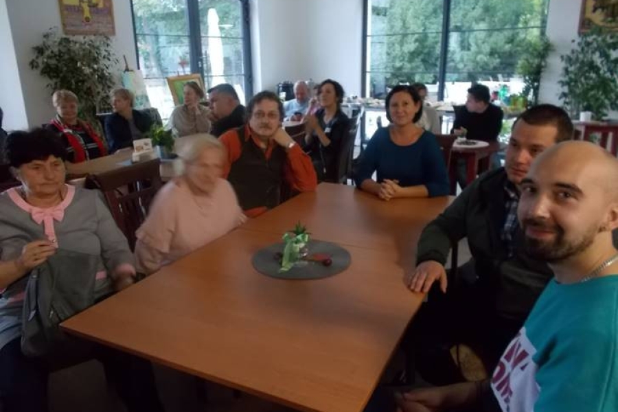 Grupa uczestników wraz z terapeutką siedzący przy stolikach