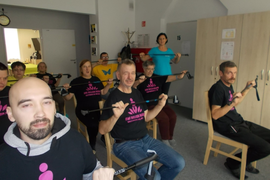 Siedzący uczestnicy podczas ćwiczeń grupowych z kijkami