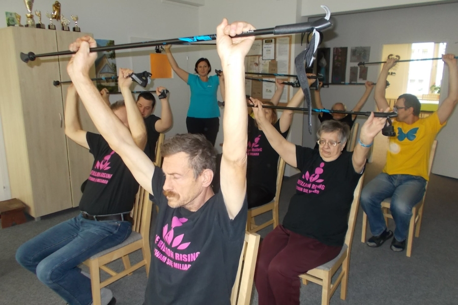 Siedzący uczestnicy podczas ćwiczeń grupowych z kijkami