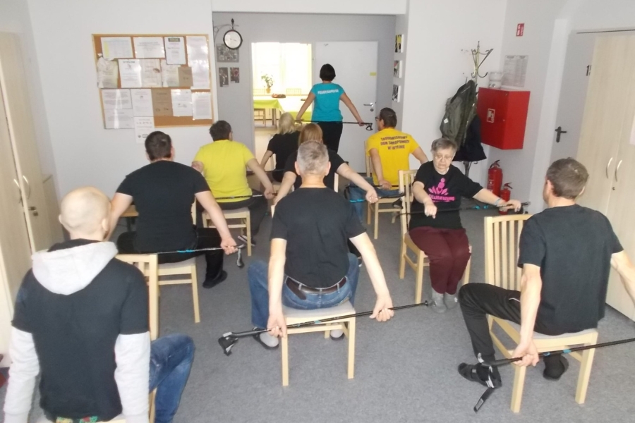 Uczestnicy siedzący tyłem podczas ćwiczeń z kijkami