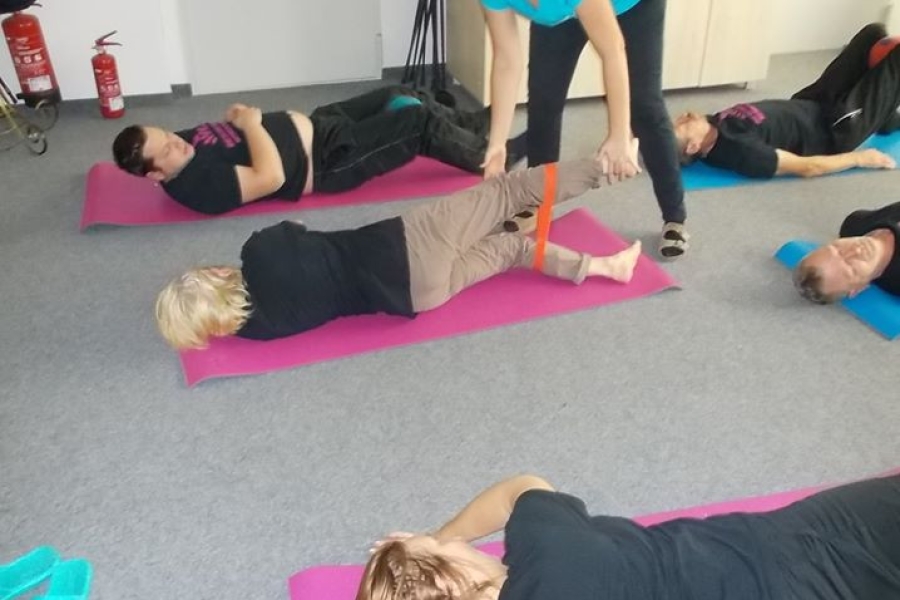 Uczestnicy leżący bokiem na karimatach wykonujący ćwiczenia z gumą