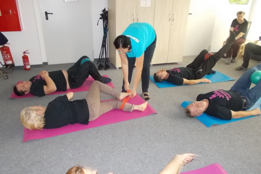 Uczestnicy leżący bokiem na karimatach wykonujący ćwiczenia z gumą