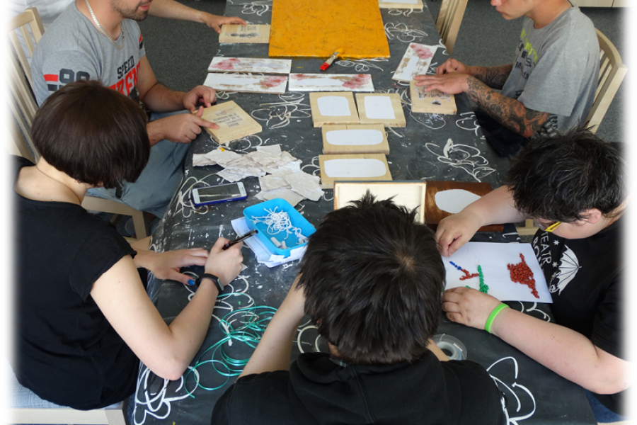 Grupa uczestników pochylona nad swoimi pracami z drewna i papieru.