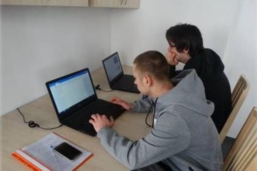 Dwóch uczestników siedzi przy biurku używając laptopów. 