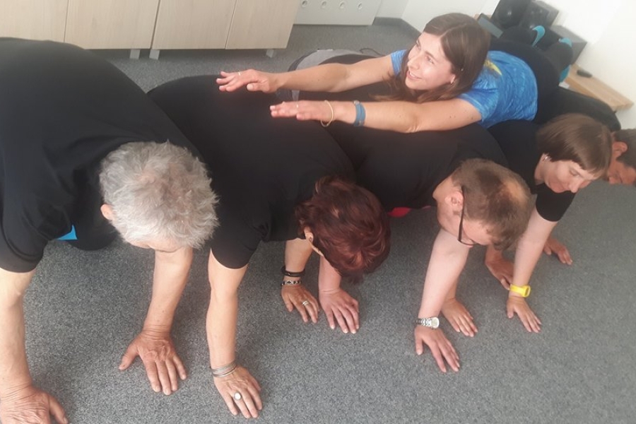 Uczestnicy w pozycji na klęczkach a na ich plecach terapeutka 