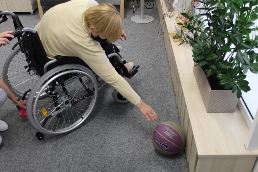 Uczestniczka siedząca na wózku inwalidzkim sięgająca piłkę.