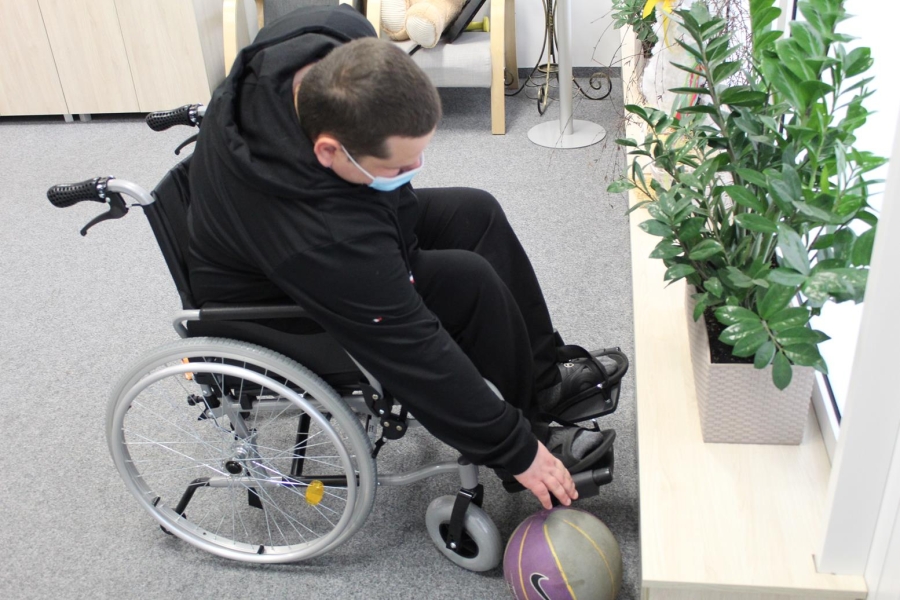 Uczestnik siedzący na wózku inwalidzkim sięgający piłkę.