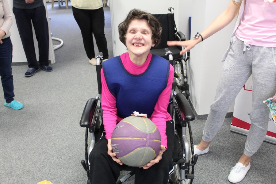 Uczestniczka siedząca na wózku inwalidzkim pozuje do zdjęcia trzymając piłkę.