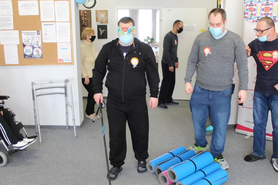 Uczestnik w asyście terapeuty pokonujący tor przeszkód z zasłoniętymi oczami.
