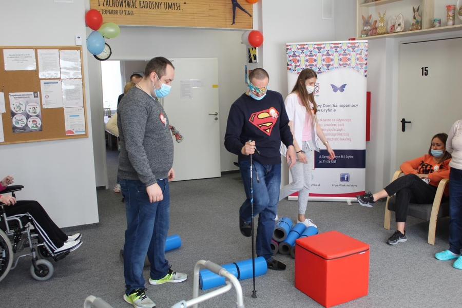 Uczestnik w asyście terapeuty pokonujący tor przeszkód z zasłoniętymi oczami.