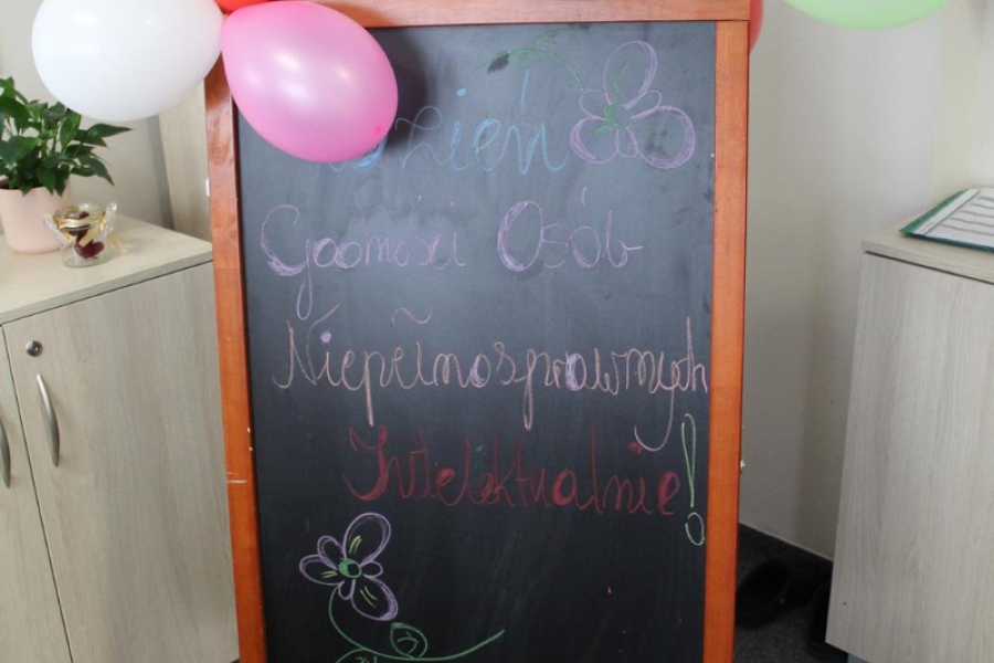 Ozdobiona balonami tablica kredowa z napisem  Dzień Osób z Niepełnosprawnością.