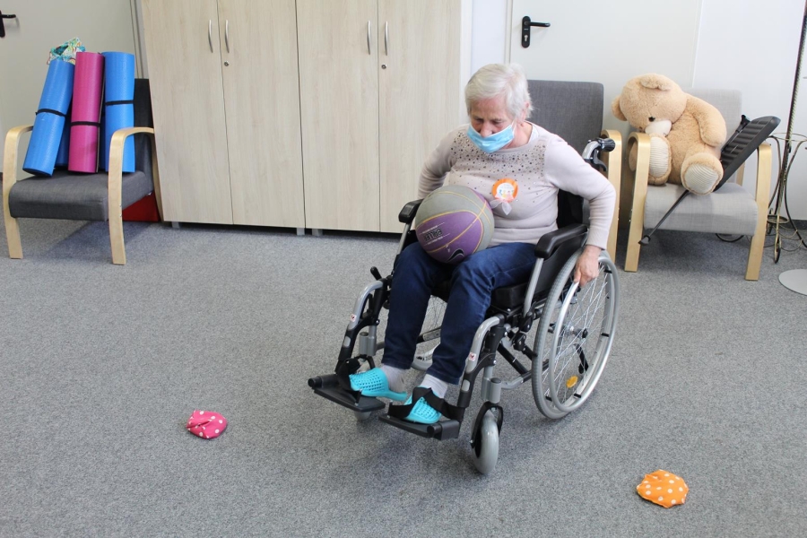 Uczestniczka wykonująca slalom na wózku inwalidzkim z piłką na kolanach