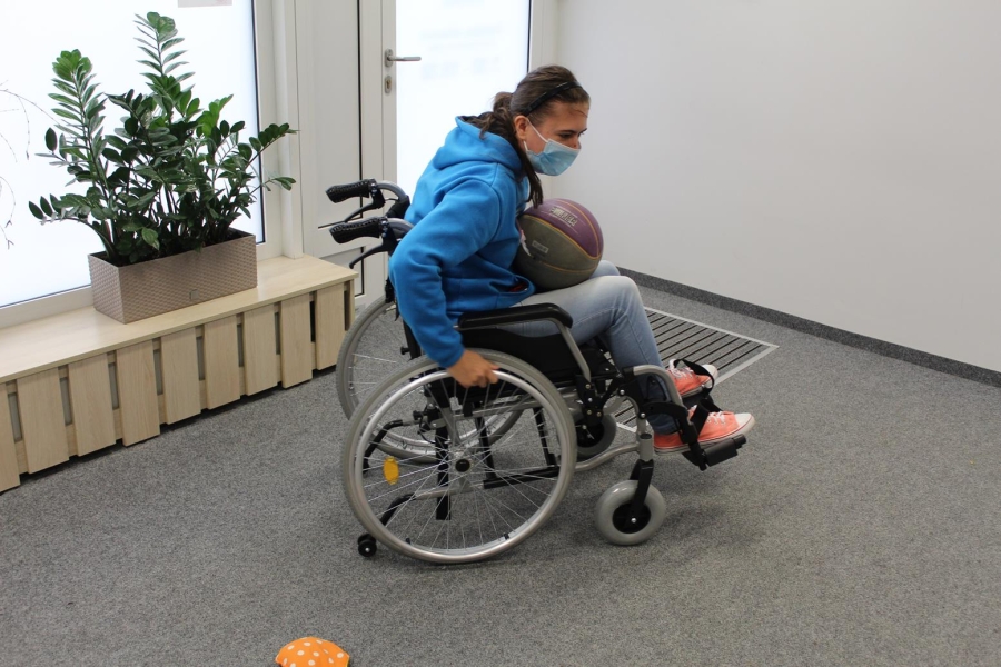 Uczestniczka wykonująca slalom na wózku inwalidzkim z piłką na kolanach.