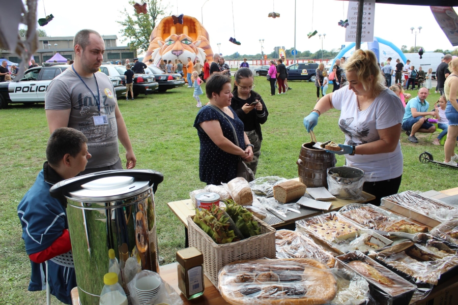 6 – Uczestniczka nakładająca ogórki na tackę na tle pikniku. 