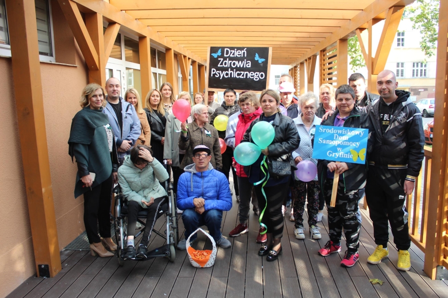 1 – Uczestnicy, Pani Kierownik oraz kadra ŚDS w Gryfinie pozują do zdjęcia trzymają transparenty na tle tarasu. 