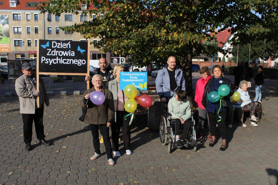 3 – Grupa Uczestników wraz z terapeutami trzymający transparent pozują do zdjęcia na Placu Barnima w Gryfinie.